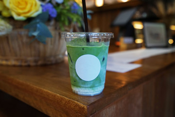 Close up plastic take away cup of Iced Matcha green tea with milk on wooden table