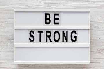 'Be strong' words on a lightbox on a white wooden surface, top view. Overhead, from above, flat lay.