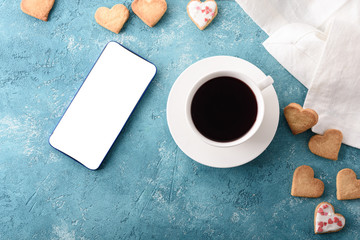 top view morning tea or coffee with homemade cookies hearts with white smartphone screen on turquoise blue table with white kitchen towel