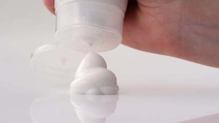 Close up studio shot of hand of unrecognizable person squeezing hydrating facial cream out of tube on white table