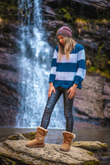 A thoughtful straight-haired blonde girl in a blue and white wool sweater in a waterfall. Lifestyle session