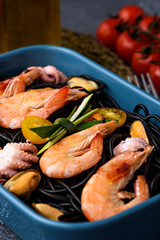 close-up of black paste with cuttlefish ink with seafood-shrimps, mussels, octopuses, tomatoes in blue plate on the kitchen table