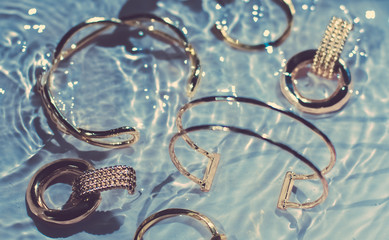 Golden bracelets, earrings, rings, jewelery on blue water background, luxury glamour and holiday...