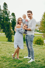 A young and beautiful blonde mother in a blue dress, along with her handsome man dressed in a white...