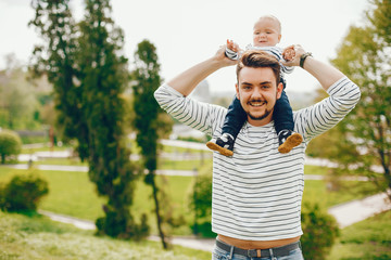 Naklejka premium beautiful tall and stylish father in a sweater and jeans is pounding with his little sweet son in a sunny summer park