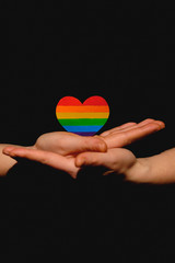 Female arms holding the heart coloured in LGBT pride colours on the dark background. Concept of the International Day Against Homophobia concept, sexual equality, feminism, social safety