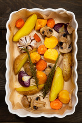 Roasted vegetable with rosemary on backing paper in a dish on wooden dark brown background.