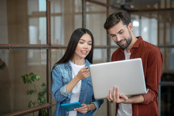 Beraded handsome man in a brown shirt and his female colleague looking at the laptop