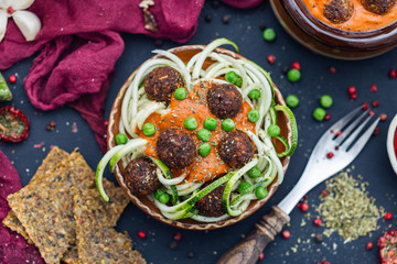 Bowl of raw vegan meat balls surrounded with vegetables and raw bread on a dark tabletop flat lay....