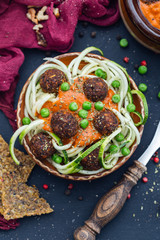 Bowl of raw vegan meat balls surrounded with vegetables and raw bread on a dark tabletop flat lay. Veggie meatballs with zucchini and peas and red sauce.