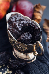 Dehydrated plums in a silver cup on a dark tabletop. Flat lay scene with dried plums
