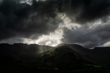 Obraz na płótnie Canvas Stormy skies and a bright sun trace light over The Langdale Pikes in the English Lake District