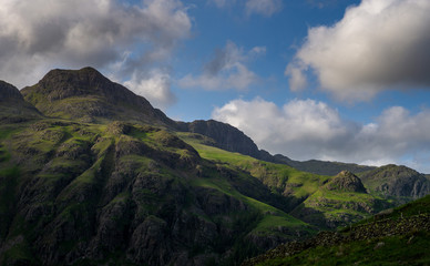 Naklejka premium Stormy skies and a bright sun trace light over The Langdale Pikes in the English Lake District