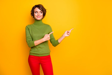 Photo of beautiful lady indicating fingers looking cunning empty space advising black friday low prices wear casual green turtleneck red trousers isolated yellow color background