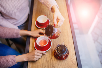 Person pouring tea with rose flowers on white table