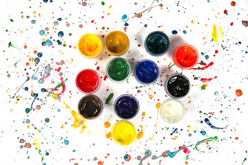 Jars with gouache paints on colorful paint splashes background. Plastic cans with multi-colored dye...