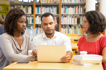 Front view of thoughtful people working at library. Focused students studying with laptop at library. Education concept