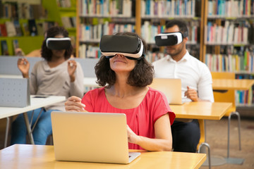 Cheerful Caucasian woman wearing VR headset. Smiling mature user with virtual reality glasses in library. Technology concept
