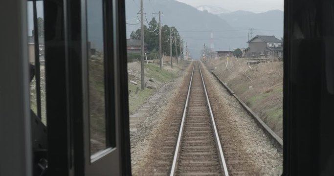 Pov driving forward facing view from train in Japan. Railroad railway line in counrtyside with mountains at background.