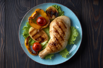 Grilled chicken leg with vegetables on a blue plate