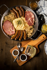 Sauerkraut Pfanne mit Nürnberger Rostbratwürste, Kassler Nacken,  Kartoffelpüree und Senf auf Holz Tisch