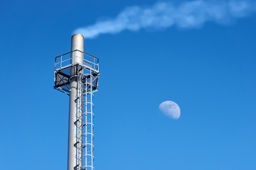 High chimney made of stainless steel of an industrial gas boiler with smoke coming out of it (steam). Steel platform and vertical ladder for maintenance.