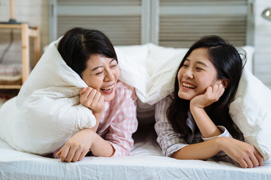 two asian korean best friends tell secrets in bed. Group of pretty young women in pajamas lying and talking under white blanket in cozy bedroom. beautiful female laughing cheerful chatting together