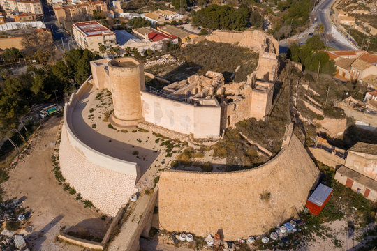 Aerial panoramic view of medieval Elda castle above the town with partially restored walls, towers and gate made of white lime stone in Spain