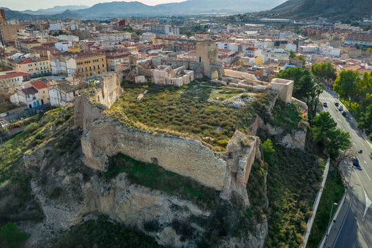 Aerial panoramic view of medieval Elda castle above the town with partially restored walls, towers and gate made of white lime stone in Spain