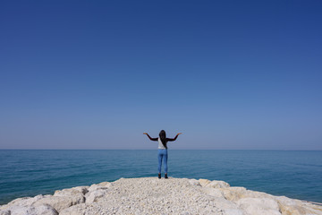 Woman standing on the seashore hands up over blue sky background, Bahrain.