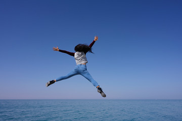 Woman open arms and legs jumping on the air over sea view and blue sky background, Bahrain. © Jantira