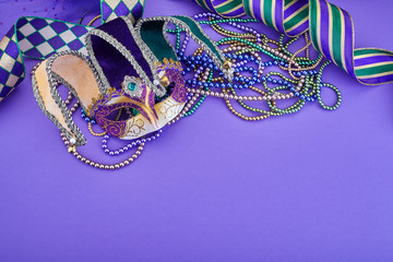 Colorful Mardi Gras mask on purple background with beads and ribbons. Top view. Copy space