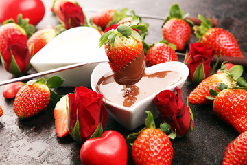 Valentine Chocolate fondue melted with fresh strawberries and dark and white chocolate. Red roses and sugar hearts for Valentines Day. Valentine Background