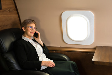 beautiful aged woman in the cabin of a private plane in an armchair with a phone in her hands