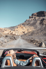 Young woman traveling by convertible car on the picturesquare road on the desert valley, rear view. Carefree lifestyle and travel concept