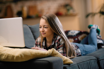 Teenage girl laying on sofa with laptop. portrait of beautiful girl at home. 