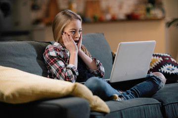 Fototapeta premium Surprised girl with laptop sitting on sofa.