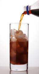 cola is poured into a glass with ice