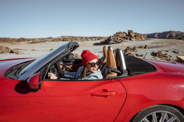 Fototapeta na wymiar Young woman traveling by convertible car on the picturesquare desert valley. Carefree lifestyle and travel concept