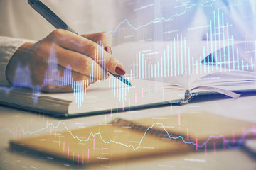 Multi exposure of woman's hands making notes with forex graph hologram. Concept stock market...