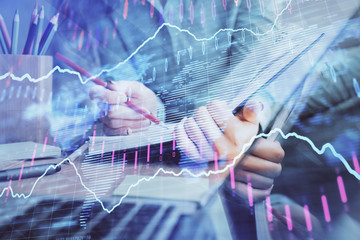 A woman hands writing information about stock market in notepad. Forex chart holograms in front. Concept of research. Multi exposure