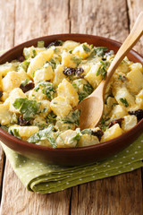 African potato salad with yogurt, herbs, spices and dried olives close-up in a bowl. vertical