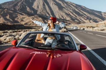 Carefree woman dressed casually in jeans and red hat enjoying road trip on the volcanic valley,...