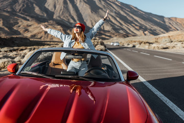 Carefree woman dressed casually in jeans and red hat enjoying road trip on the volcanic valley,...