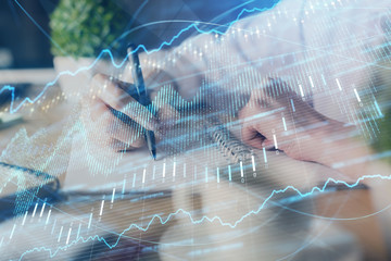Financial forex graph displayed on hands taking notes background. Concept of research. Double...
