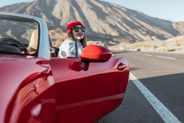 Woman in red hat traveling by cabriolet on the desert valley, getting out the car on the roadside...