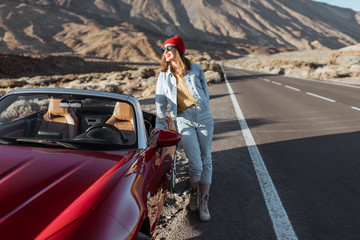 Young woman enjoying road trip on the desert valley, standing near the convertible car on the...