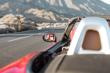 Woman driving convertible car on the beautiful desert road, view from the backside