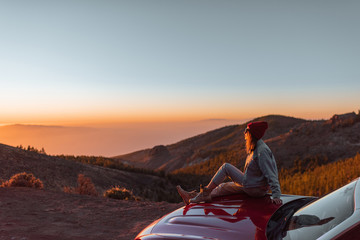 Landscape view on the roadside above the clouds with woman enjoying beautiful sunset, sitting on...