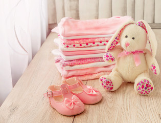 Baby clothes and baby shoes for a newborn girl in pink with a plush bunny.